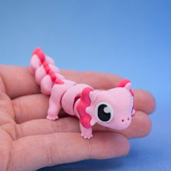 Pink axolotl fidget toy seen from the front, showing its frilly gills and large eye