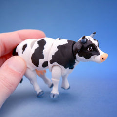 Black and white cow fidget toy with small horns, shown mid-stride
