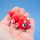 Cera the Dino Hatchling triceratops fidget toy in red, with white petal-like horns and white back spikes, curled in a hand