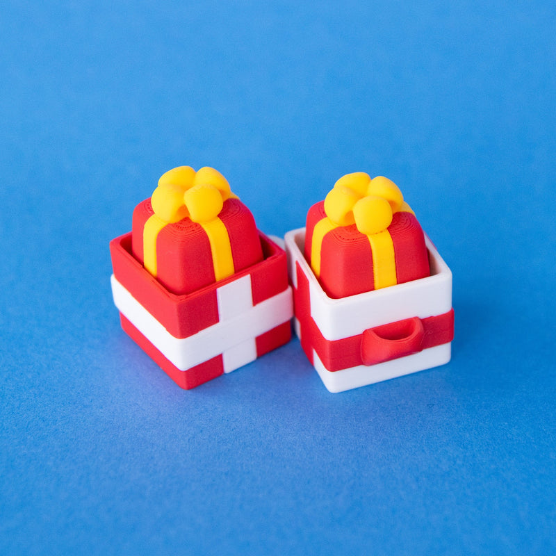 Red and white single gift box clicker bases, each holding a red present keycap with a yellow bow