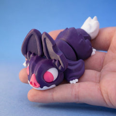 Purple bat-themed chonk dragon fidget toy with large ears and a pink nose, curled in a hand