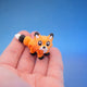 Orange fox fidget toy with black paws and a white-tipped tail, standing on fingers
