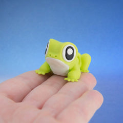 Lime green frog fidget toy with big round eyes, crouched on fingers