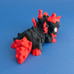 Rear three-quarter view of Gritt the Lava Chonk showing the red tail and cracked black body.