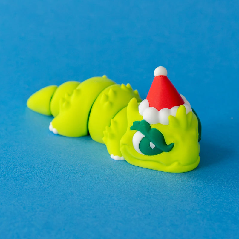 Grump the Humbug Chonk lying flat in his Santa hat, front left view