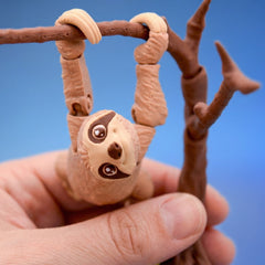 Sloth fidget toy hanging upside down from a branch by its curved claws, face turned toward the camera