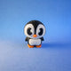 Mabel penguin figurine standing alone, showing her single white belly against a blue background.