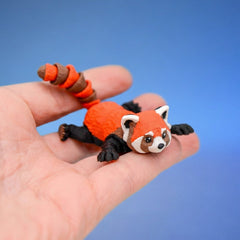 Orange and black red panda fidget toy sprawled in a hand, showing its ringed tail