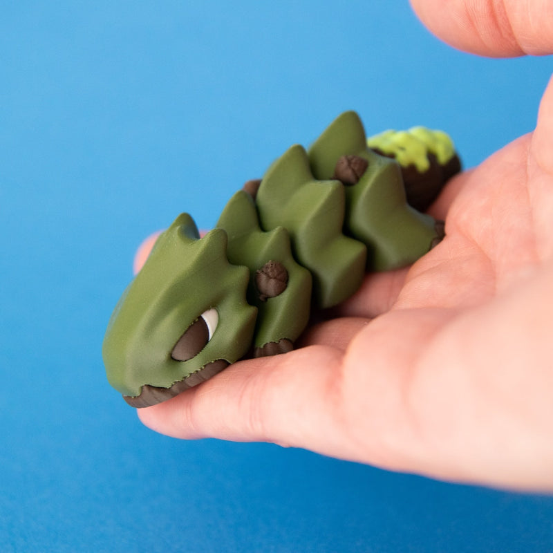 Oke held in a hand, with his face, acorns and leaf-shaped body segments visible.