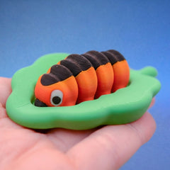 Orange and black caterpillar fidget toy with a chunky body, resting on a green leaf-shaped base