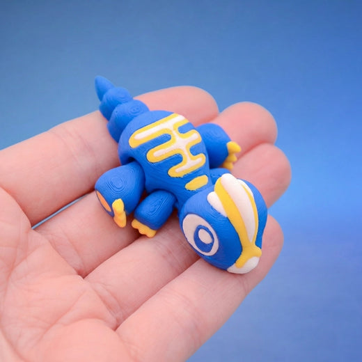 Blue dinosaur fidget toy seen from above, showing the yellow stripe pattern along its spine and curled tail
