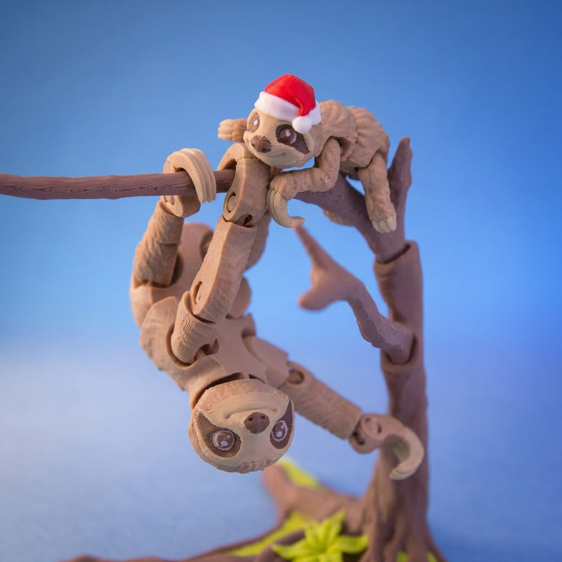 Christmas Hat Pip perched above Hugo as both sloths hang from their display tree.