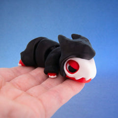 Black chonk dragon fidget toy with a hooded shape and red-rimmed eye, curled in a hand