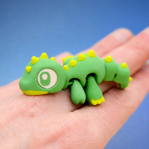 Rex the Dino Hatchling in the Spiky style - green dinosaur fidget toy with yellow back spikes, sprawled in a hand