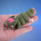 Green zombie chonk dragon fidget toy with an exposed pink brain and X-shaped eye scar, curled in a hand