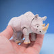 Grey rhino figurine with a tan horn, standing in a hand