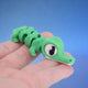 Green crocodile fidget toy with a segmented body, crawling across fingers