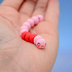 Pink and red earthworm fidget toy coiled in a palm, showing its cartoon face