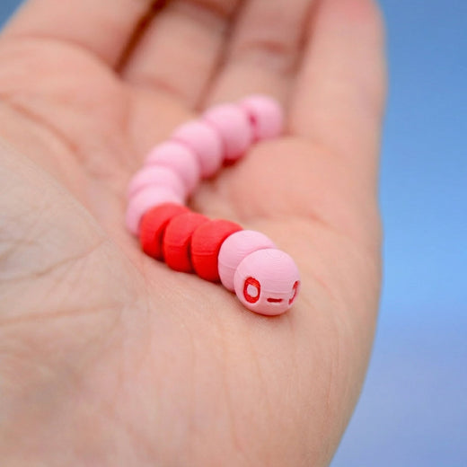 Pink and red earthworm fidget toy coiled in a palm, showing its cartoon face