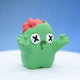 Green zombie bean fidget figurine with X-shaped eyes and a cracked-open head showing a red brain, arms raised