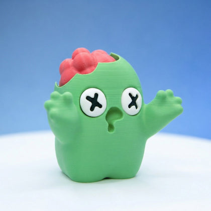 Green zombie bean fidget figurine with X-shaped eyes and a cracked-open head showing a red brain, arms raised
